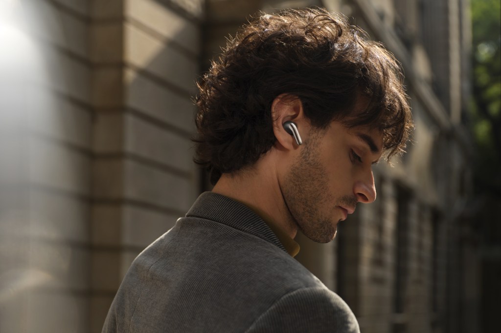 A side profile of a man with dark curly hair wearing a pair of silver Xiaomi earbuds.